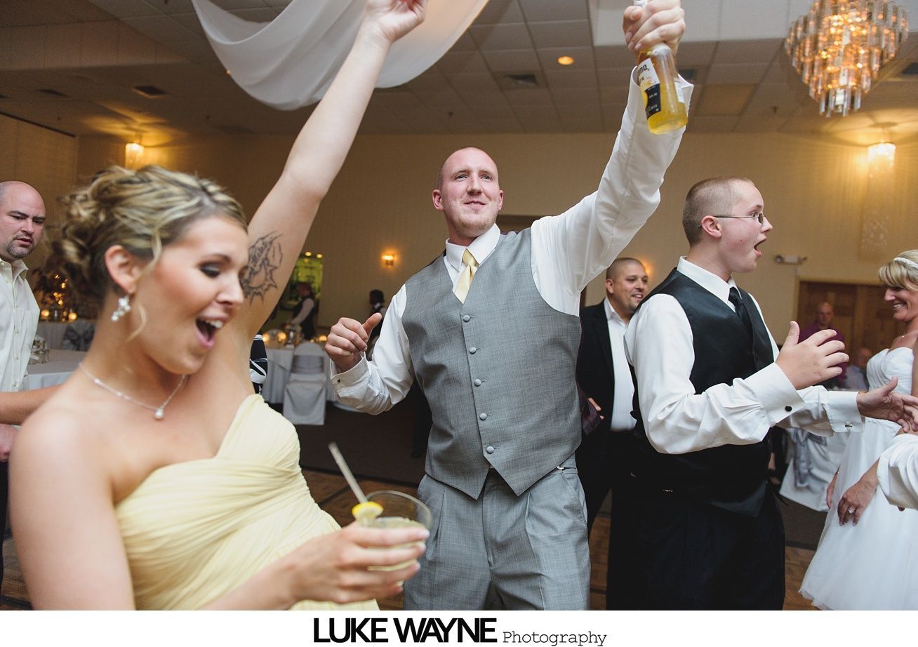 People dancing at a wedding reception; a woman with arm raised, man with champagne, in a ballroom with a chandelier.