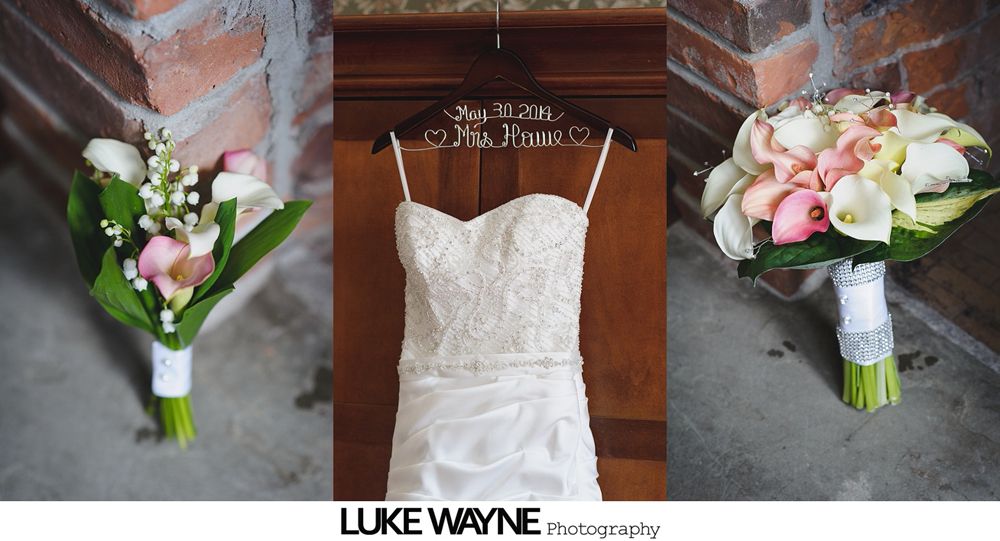 Wedding dress hanging between bouquets of flowers, brick wall background.