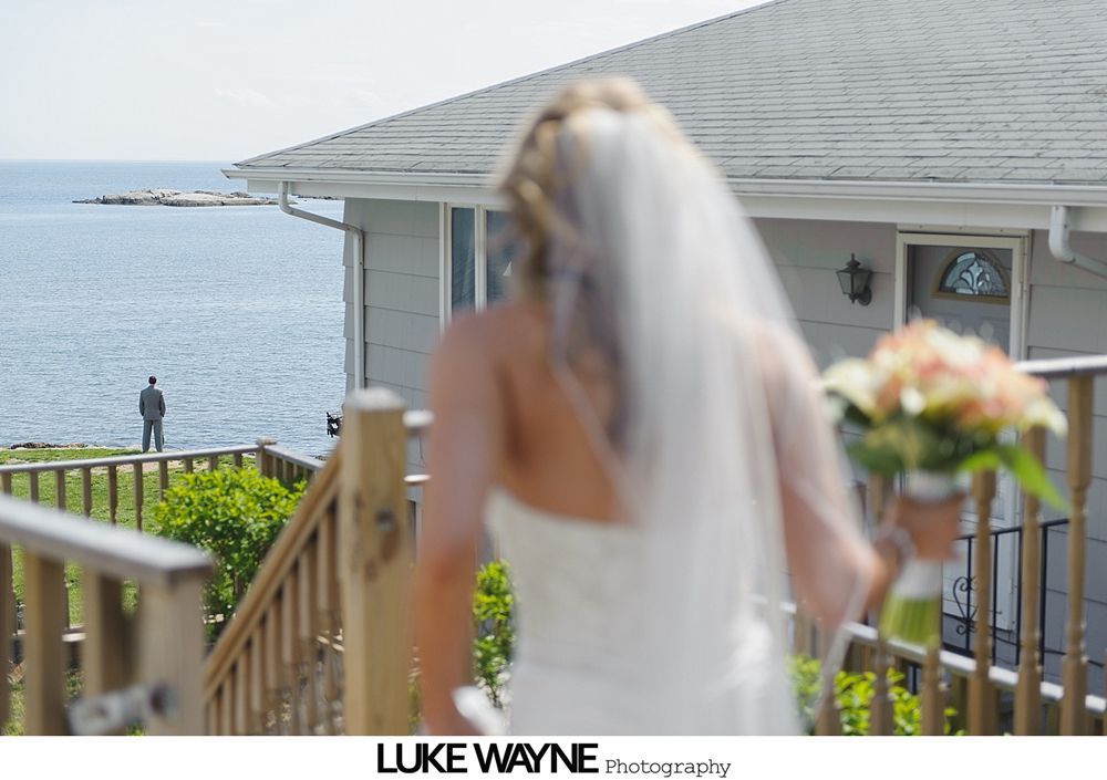 Bride walking down stairs towards groom standing by the sea. Soft focus, sunny day, bouquet in hand.