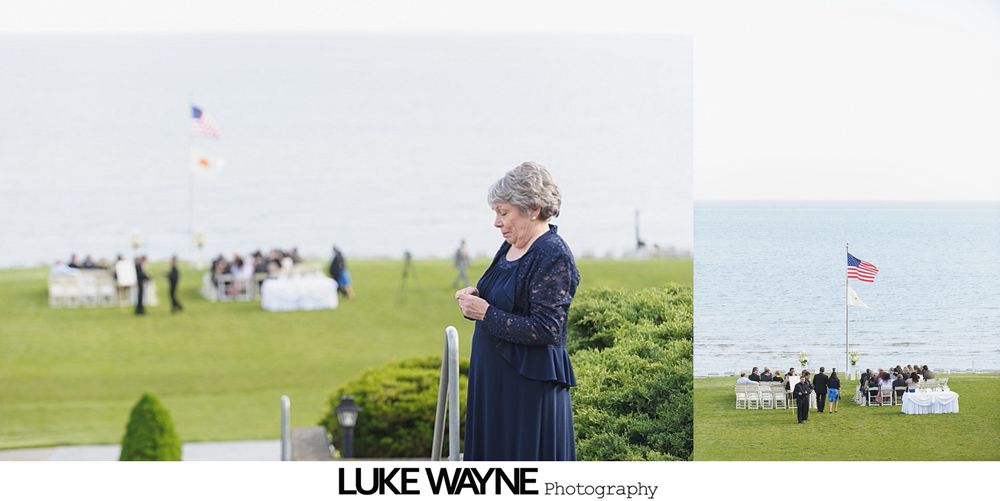 A woman in a blue dress stands on a grassy hill overlooking a ceremony with an American flag by the water.