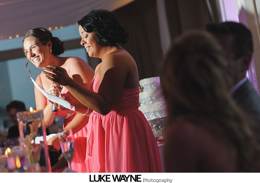 Two women in peach dresses laughing, reading at a wedding reception.