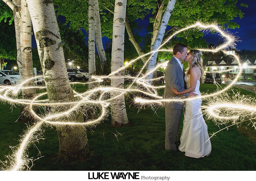 Couple kissing amidst sparkler light trails, birch trees in background, night setting.