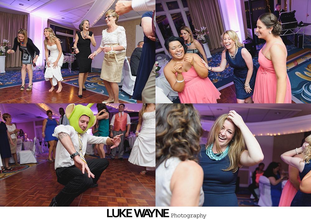 People dancing at a wedding reception, including one person in a Shrek hat, on a wooden dance floor.