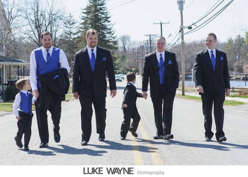 Groomsmen and two young boys in suits walk down a street. All wear blue accents.