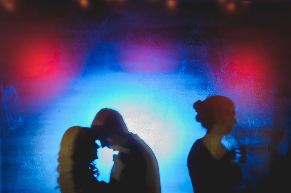 Silhouettes of a couple embracing and a person standing against a blue and red lit background.