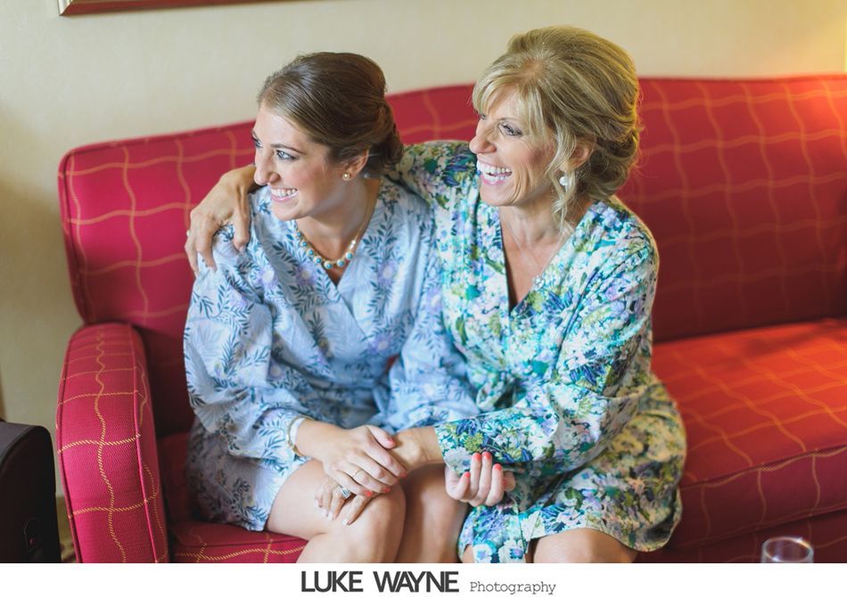 Two women in floral robes sitting on a red couch, smiling and embracing, indoors.