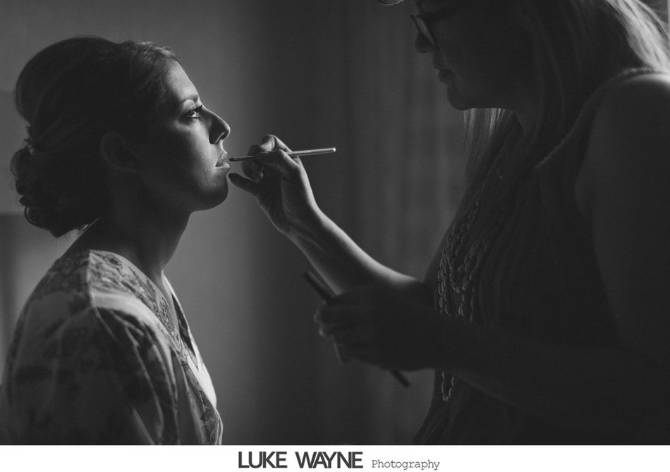 Woman having makeup applied; indoors, natural light, black and white.