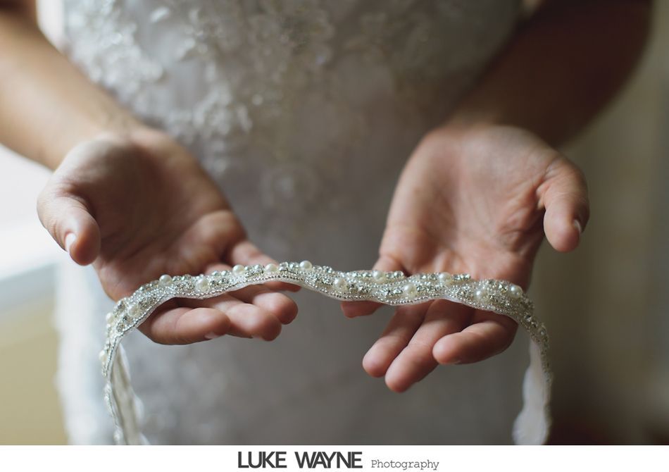 Bride's hands holding a beaded headband, white dress in the blurred background.