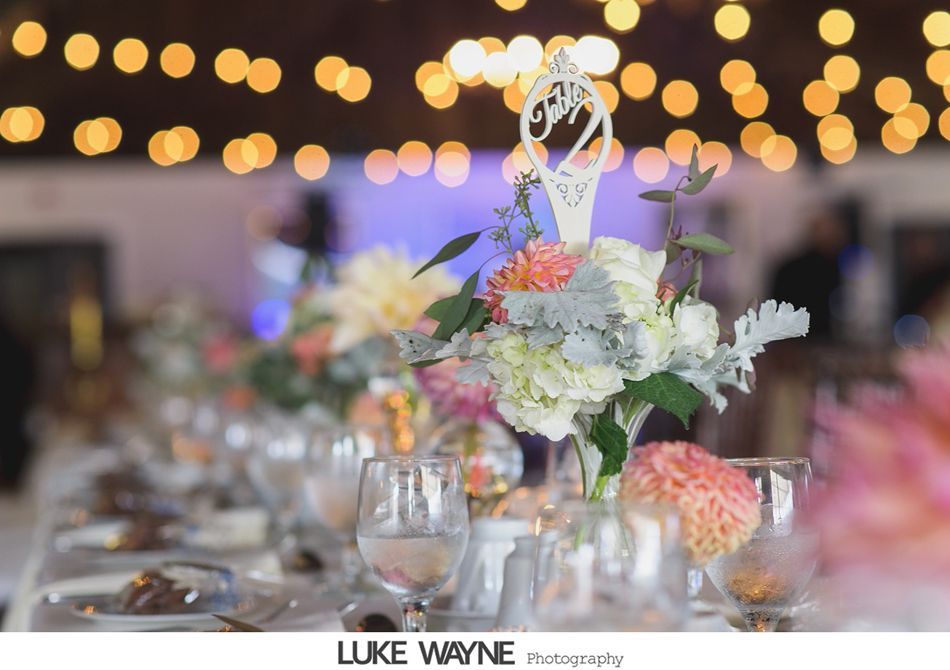 Wedding reception table setting with floral centerpiece and blurred background lights.