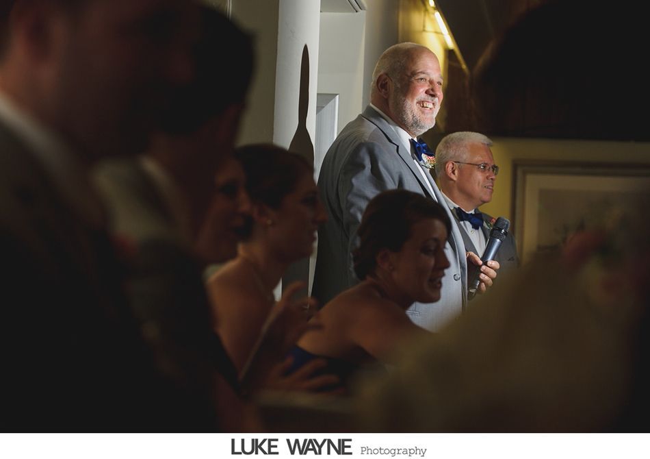 Man in gray suit smiles, standing near another man with a microphone, during a formal event.