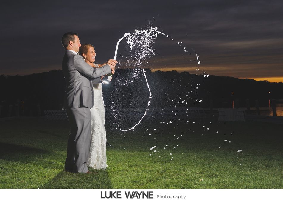 Couple sprays champagne, creating arc shape, at dusk outdoors.