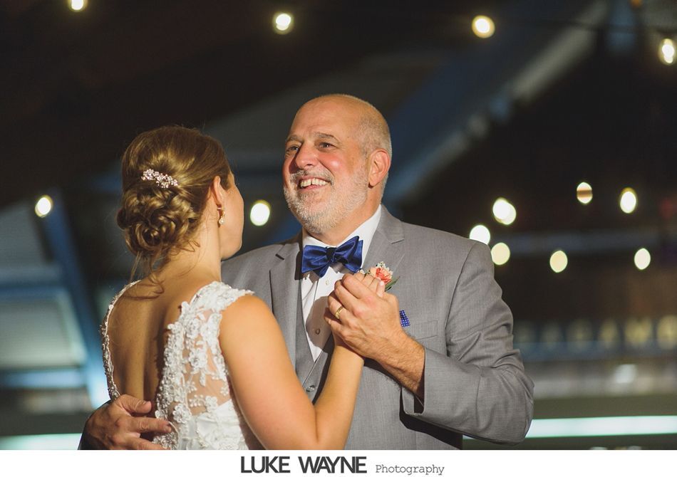 Bride dancing with father at wedding reception. Father smiles, wearing a suit and bow tie; she wears a lace dress.