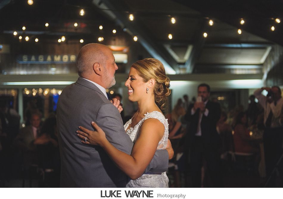 Father and bride dance at wedding reception, smiling under string lights.