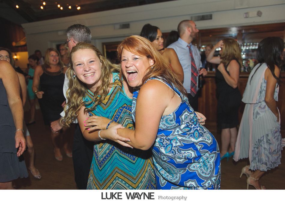 Two women laughing and embracing at a party; teal and blue patterned dresses.