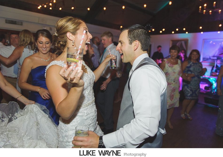 Bride and groom dancing with drinks, celebrating at wedding reception.