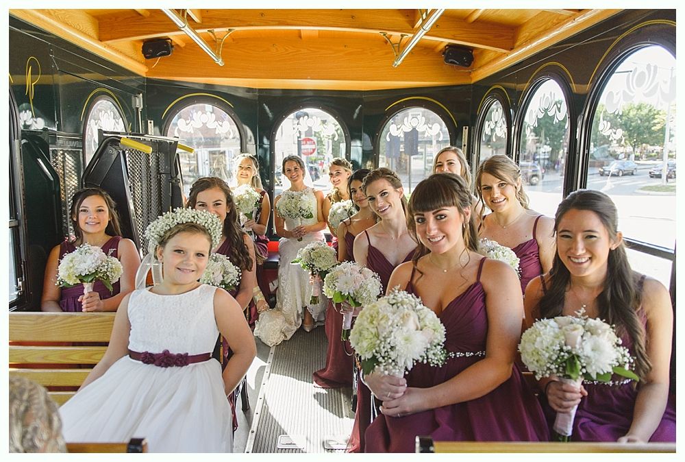 Bridesmaids in burgundy dresses and flower girl in white dress pose with bouquets in a trolley.