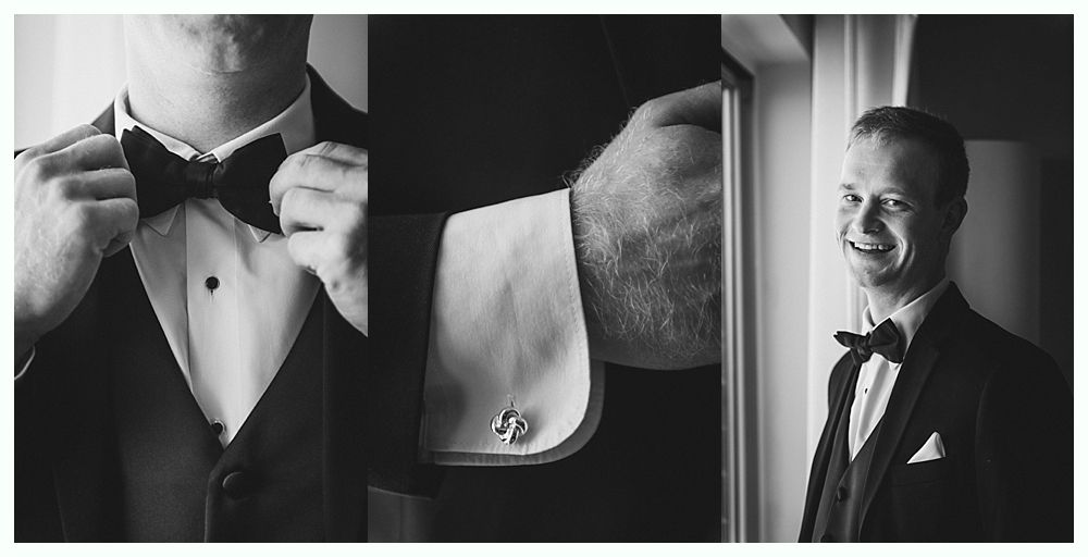 A man in a tuxedo adjusting his bow tie and cuff links, smiling.