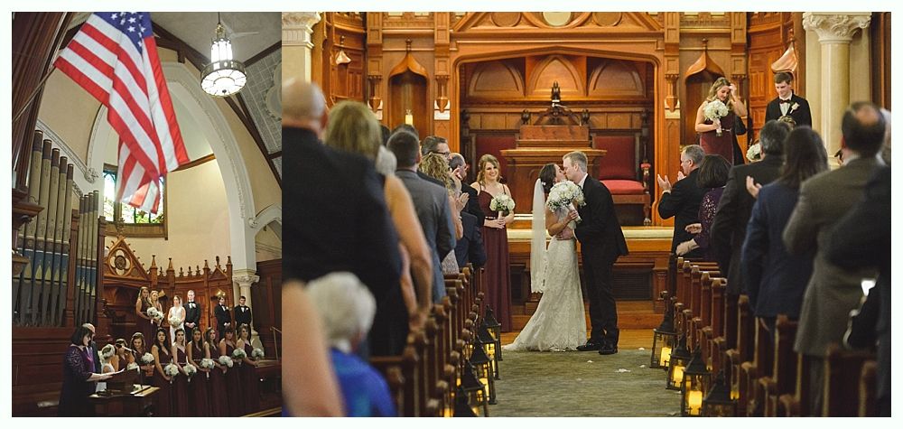 Wedding ceremony inside a church with an American flag. Bride and groom kiss at the altar as guests watch.