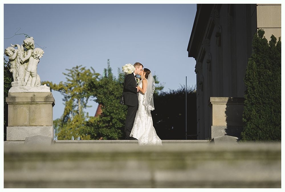 Couple kissing on wedding day near a stone building. Bride in white dress, groom in black suit.