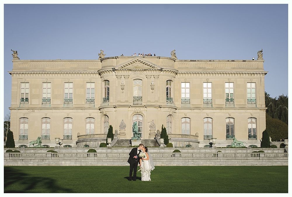 Couple kissing in front of a large mansion on a sunny day.