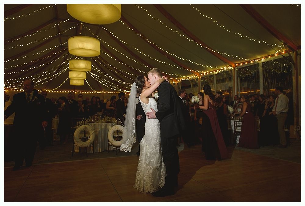 Couple dancing at a wedding reception under string lights in a tent.