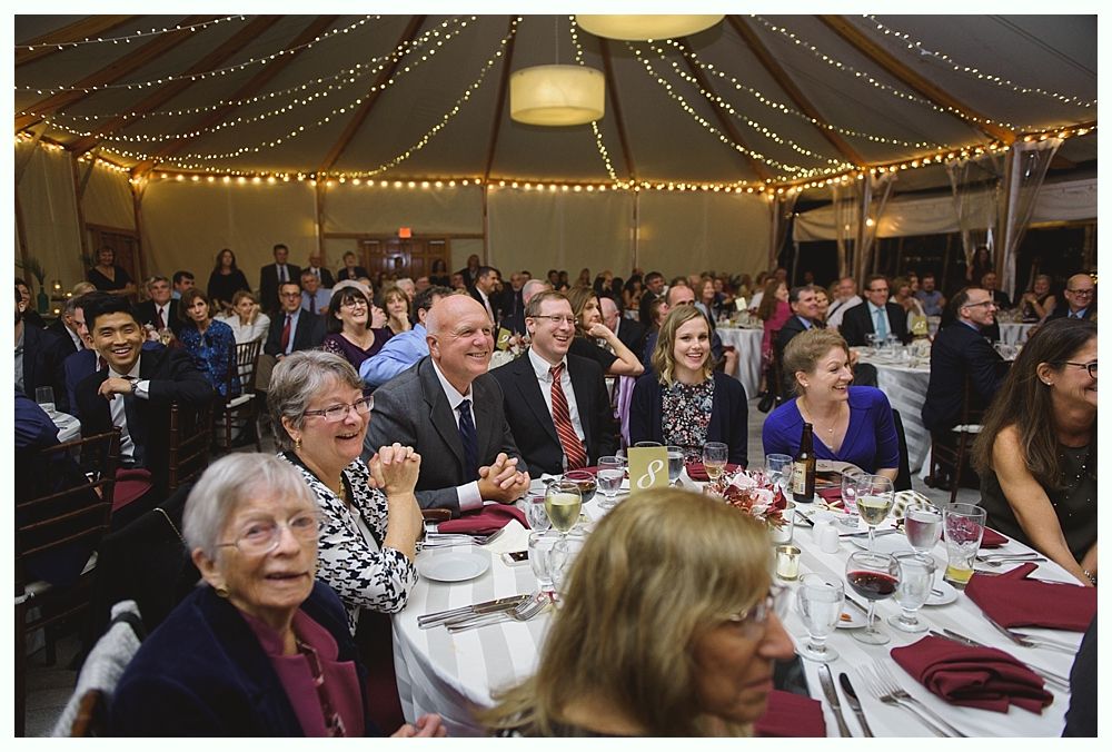 People gathered at tables in a brightly lit room, smiling and looking toward the front.