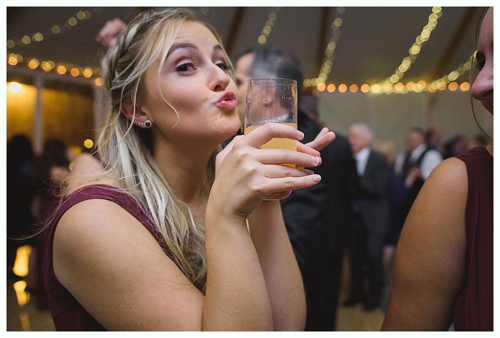 Woman puckering lips while holding a glass with an amber drink at a festive gathering.