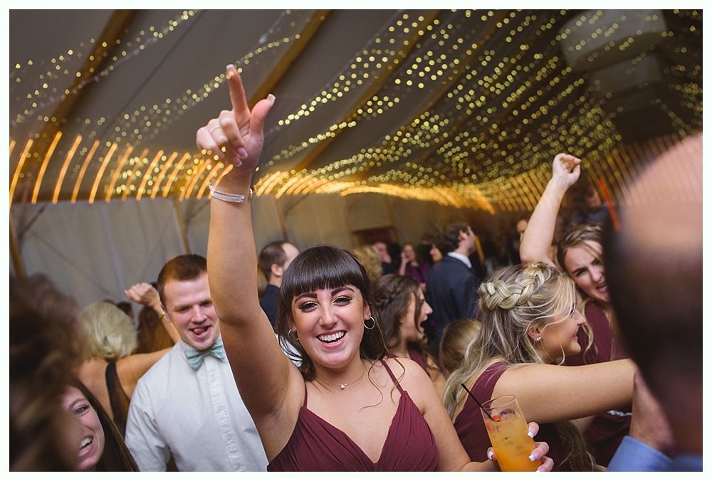 People dancing at a party under string lights; a woman in a maroon dress raises her arm with excitement.