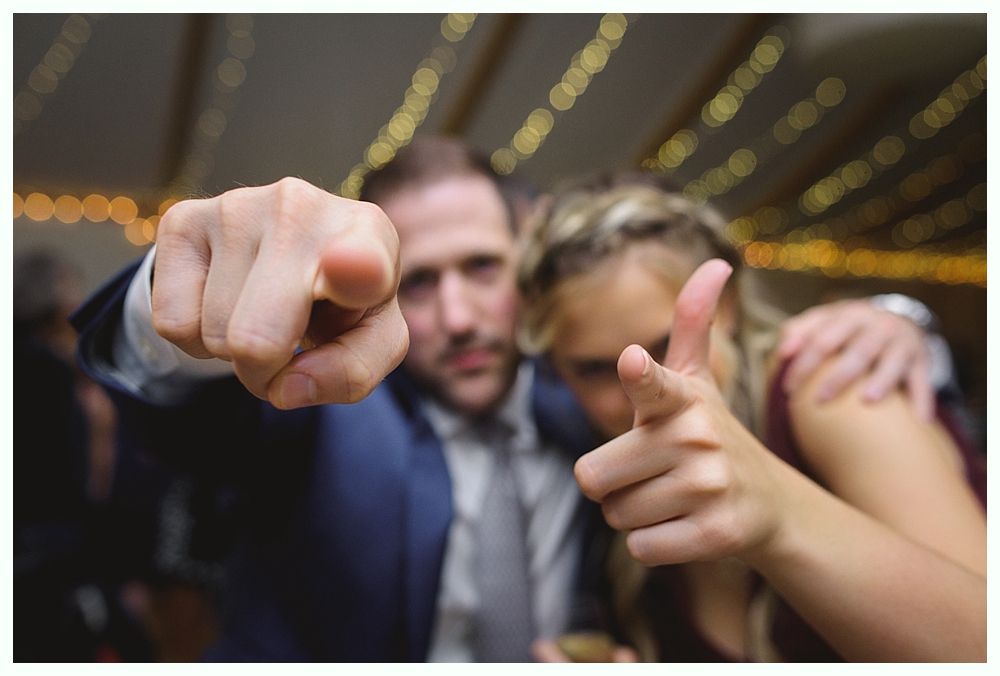 Man and woman point toward the viewer with focused expressions; blurred background with lights.