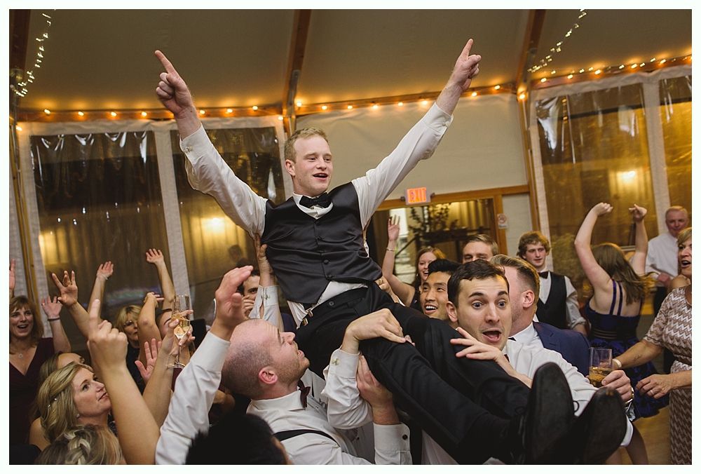 Man being held up in air by others, arms raised, celebratory mood. Indoors.