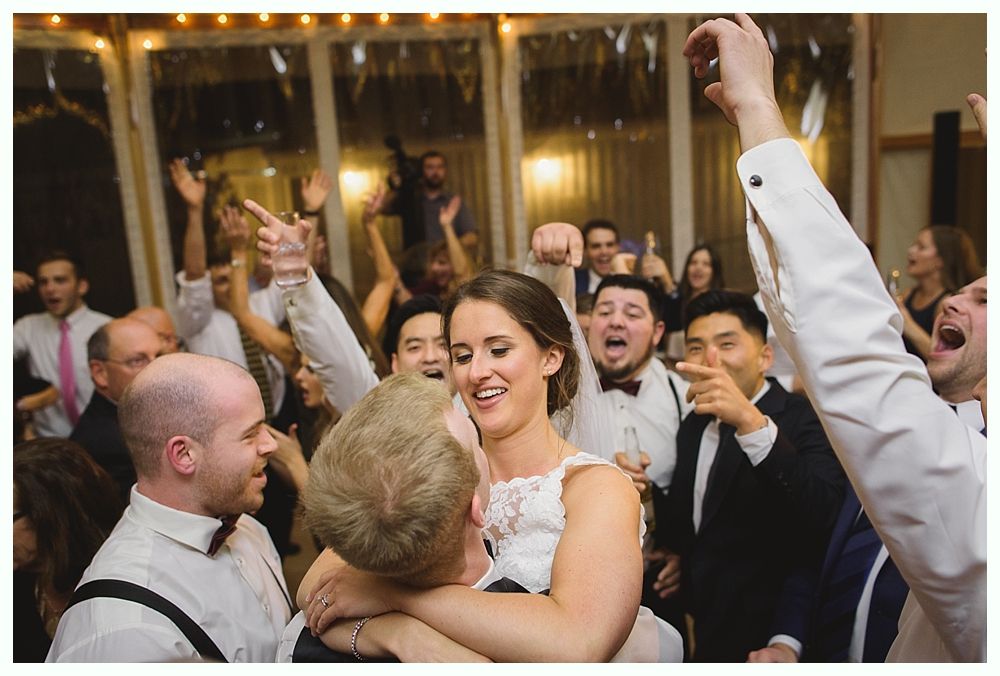 Newlyweds embraced, surrounded by cheering guests at a wedding reception.