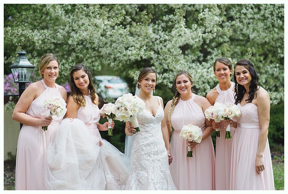 Bride and bridesmaids in pink dresses pose outdoors with bouquets.