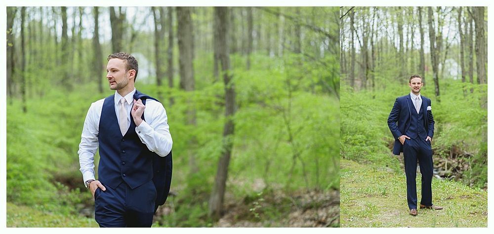 Man in a navy suit poses in a forest clearing.