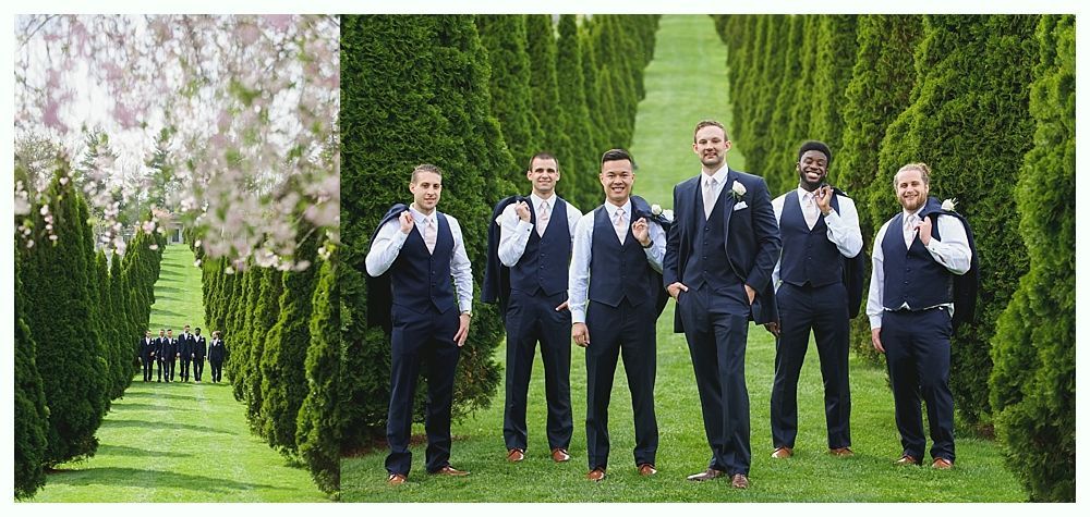 Men in navy suits stand on grass by a tree-lined pathway.