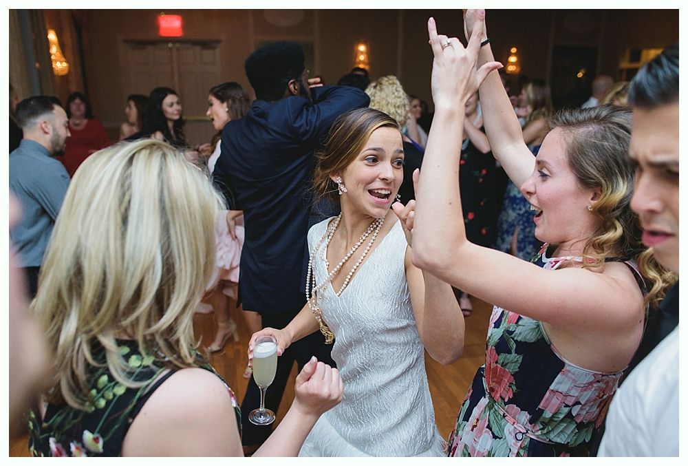 People dancing at an event. A woman in a white dress smiles while another raises her arms.