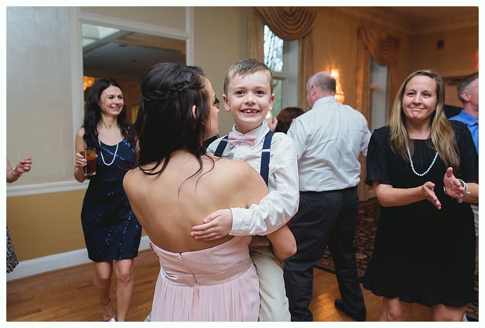 Woman in pink dress dances with a boy in a bow tie. Other people watch in a ballroom.