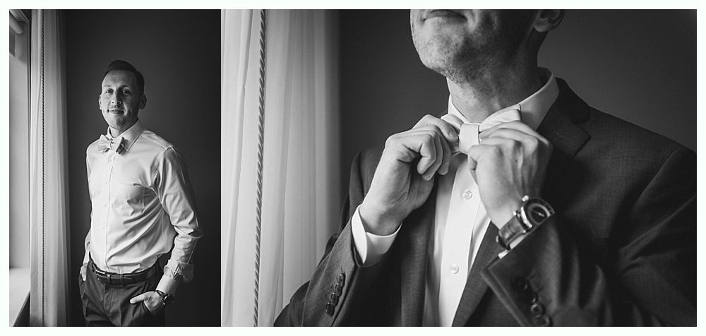 Man adjusting tie, another man in background near a window. Black and white.