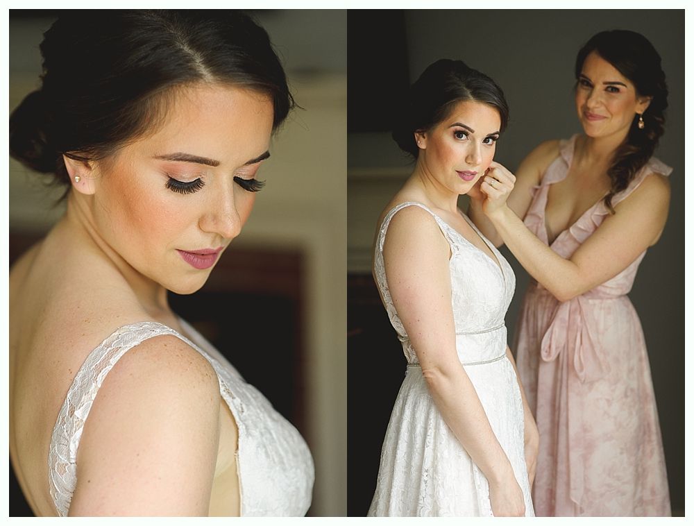 Bride in wedding dress, being helped by bridesmaid, both in a bright room.