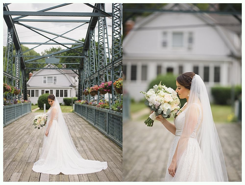Bride in a white dress on a bridge, holding a bouquet, with a house in the background.