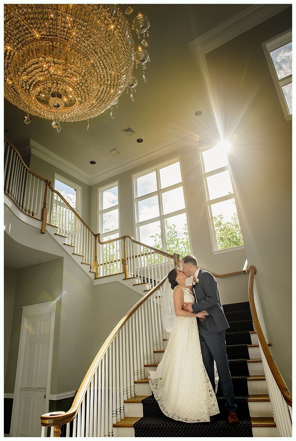 Couple kissing on a staircase, radiant sunlight, and chandelier.