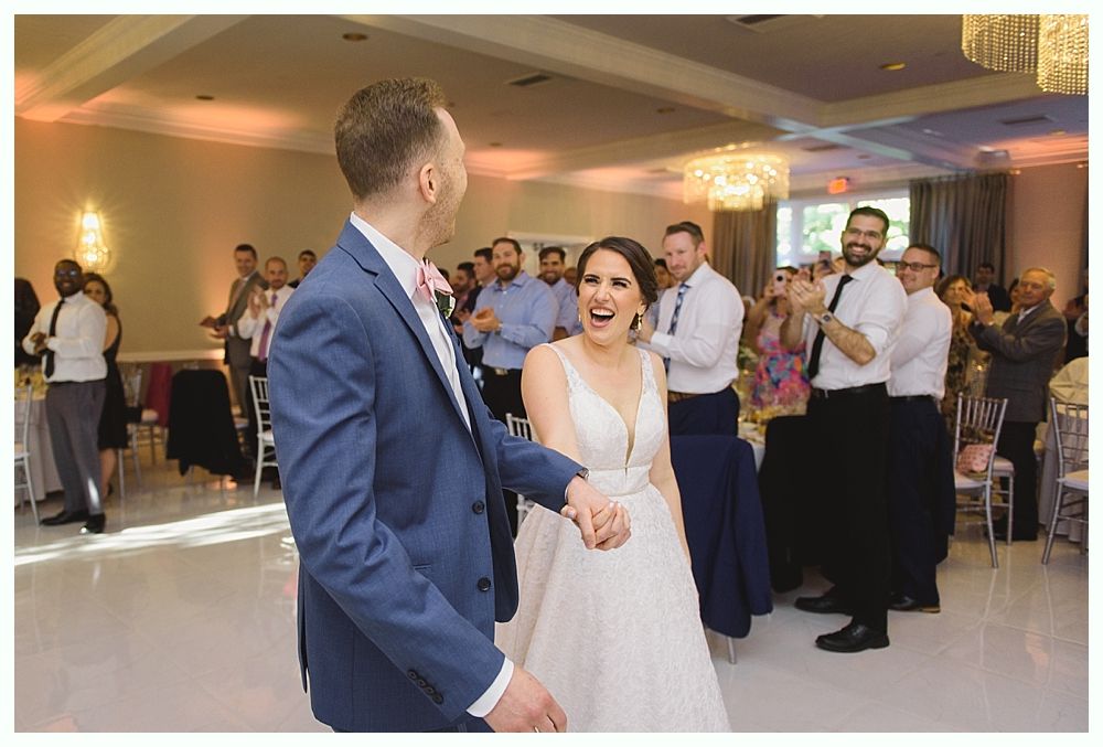 Bride and groom dancing at a wedding reception, smiling, surrounded by guests clapping.