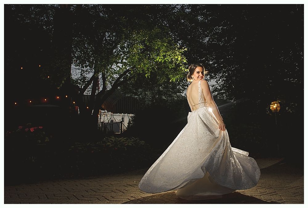Bride twirls in wedding dress outdoors at dusk, with trees and soft lighting in the background.