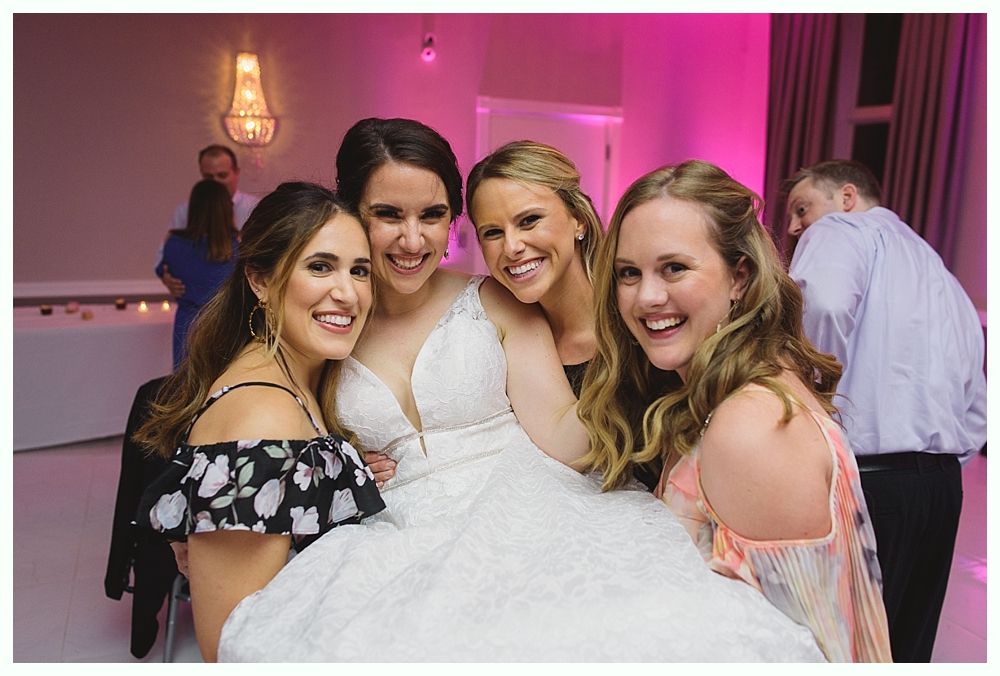 Bride and three smiling women pose together, white dress, in a well-lit room.