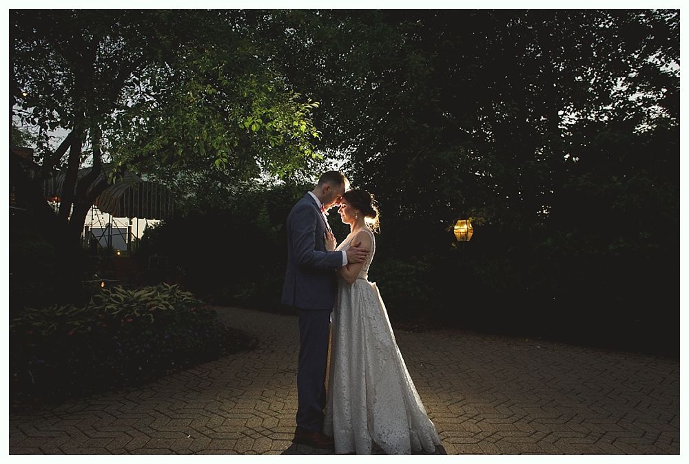 Couple embracing in wedding attire under a tree, illuminated by soft light.
