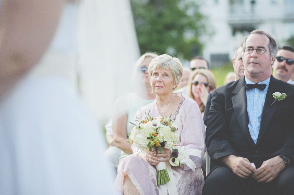 Newlyweds walk down aisle holding hands, sunflowers, gazebo in background.