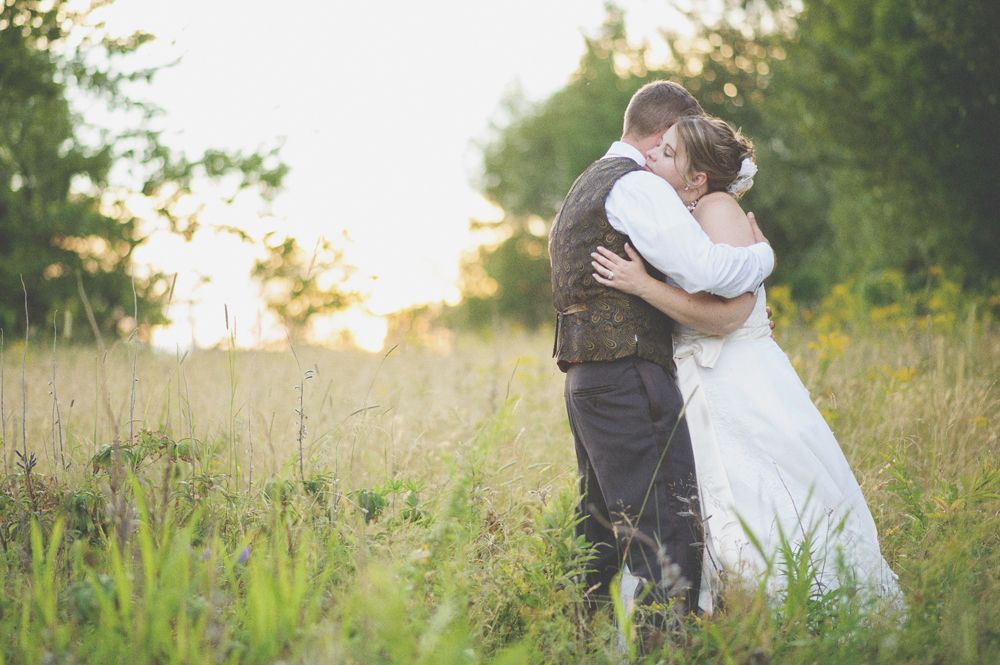Bride and groom embracing, silhouetted under a large tree, in black and white.