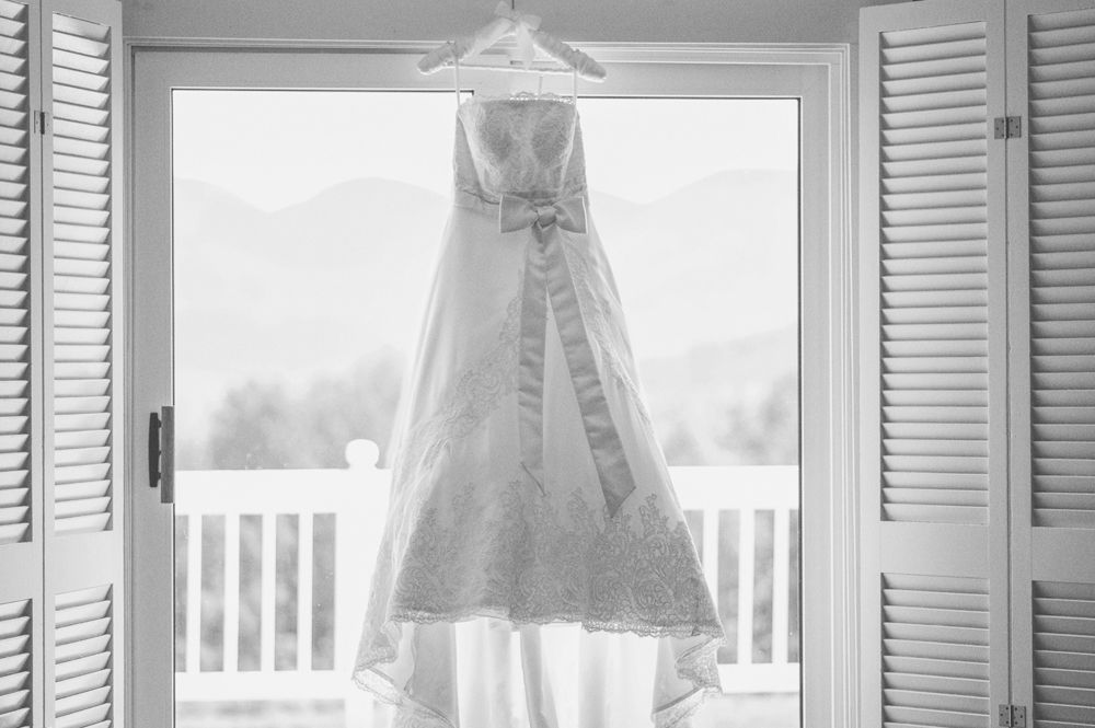 A bride is helped into her wedding dress. A bridesmaid fastens the corset back. The bride's shoes are visible.