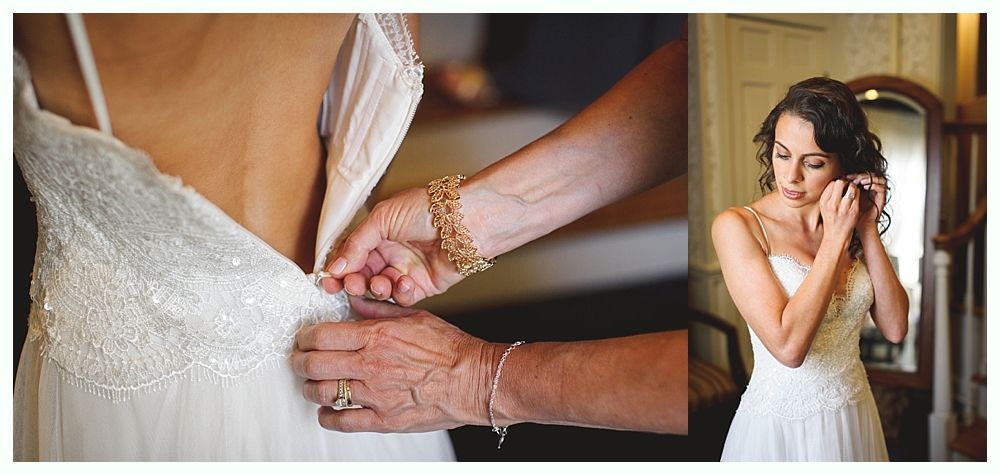 Bride getting help with her dress. A woman buttons the back of the wedding dress while the bride adjusts her earring.