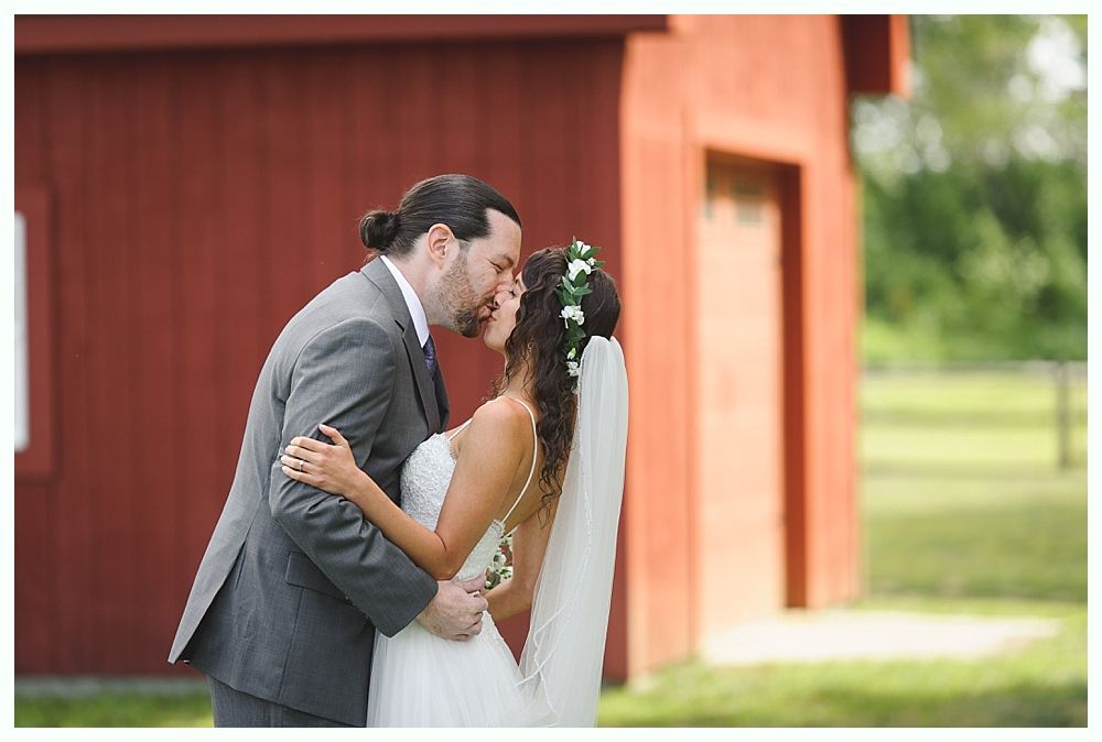 Couple kissing in front of a red barn; the woman wears a veil and flower crown.