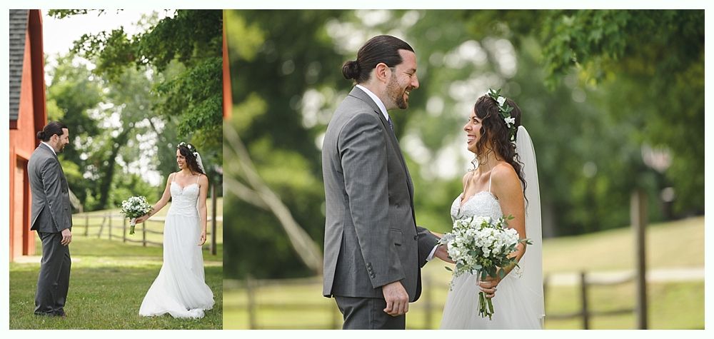 Bride and groom at outdoor wedding, smiling at each other. Man in gray suit, woman in white dress, holding flowers.